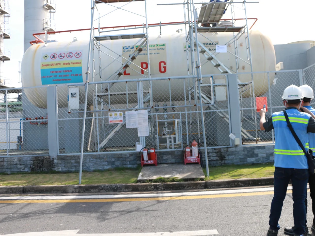 Cuve horizontale marquée GPL dans une station clôturée, avec échafaudage et deux techniciens en inspection sur le site industriel